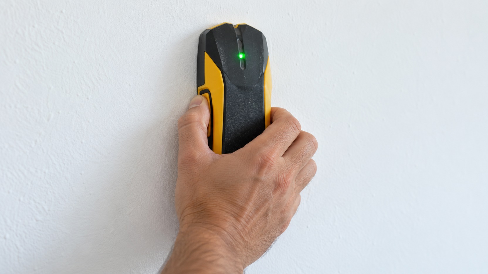 Persona deslizando lentamente un detector de pared plano sobre una zona de referencia mientras anota las lecturas