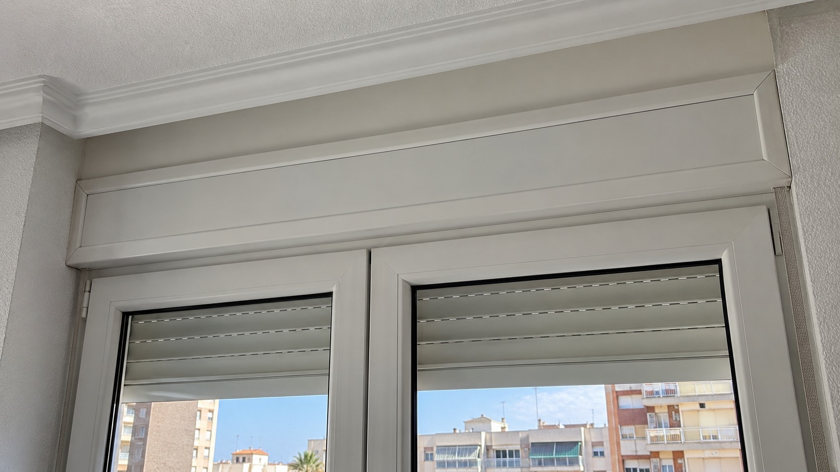 Ventana de doble cristal observada desde el interior en un día ventoso, con el cajón de persiana visible y sin abrir tapas